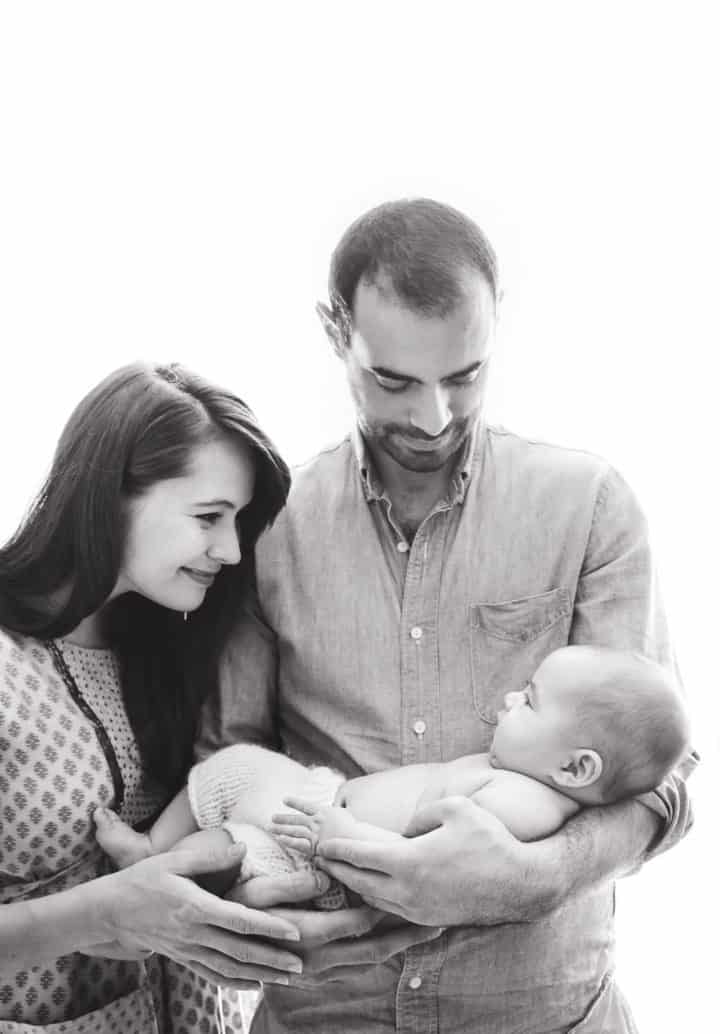 Family with 3 month old baby boy in front of a window in a black and white photo